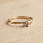 A gold ring with a diamond set in the center, resting on a wooden surface.