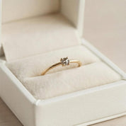 A gold ring with a diamond set in the center is displayed in a white jewelry box.