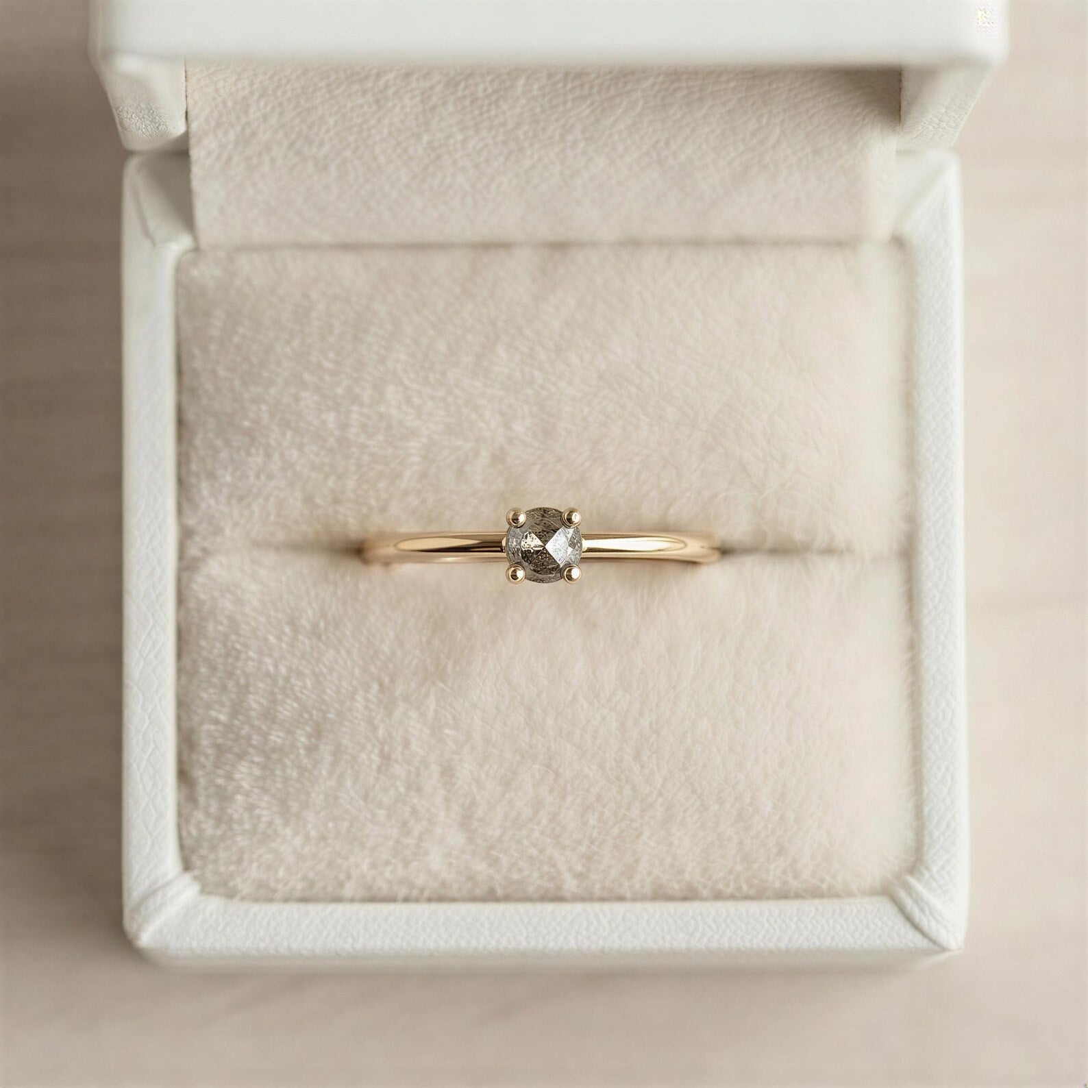 A gold ring with a diamond set in the center, displayed in a white jewelry box.