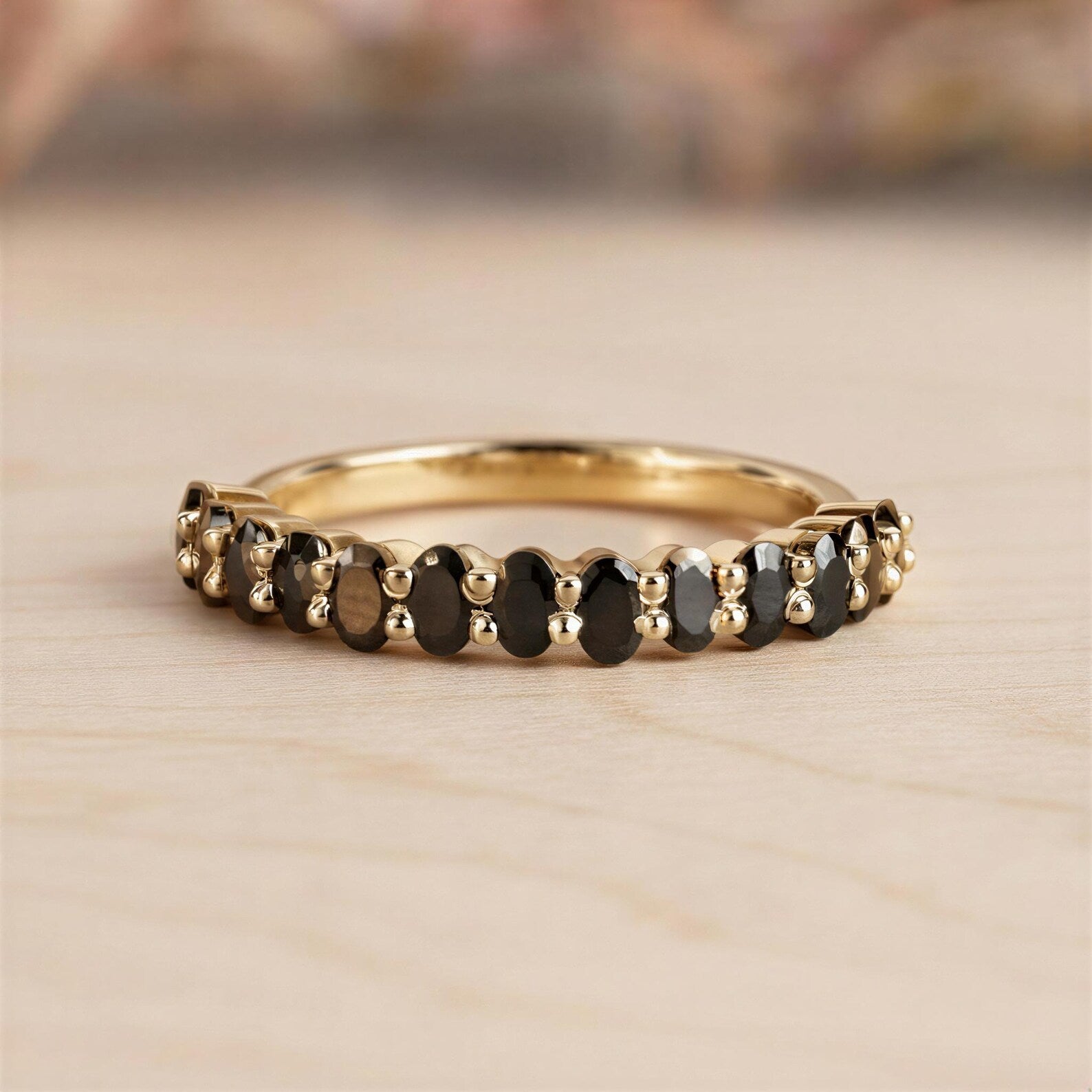 A gold ring with a row of black diamonds set in it, resting on a wooden surface.