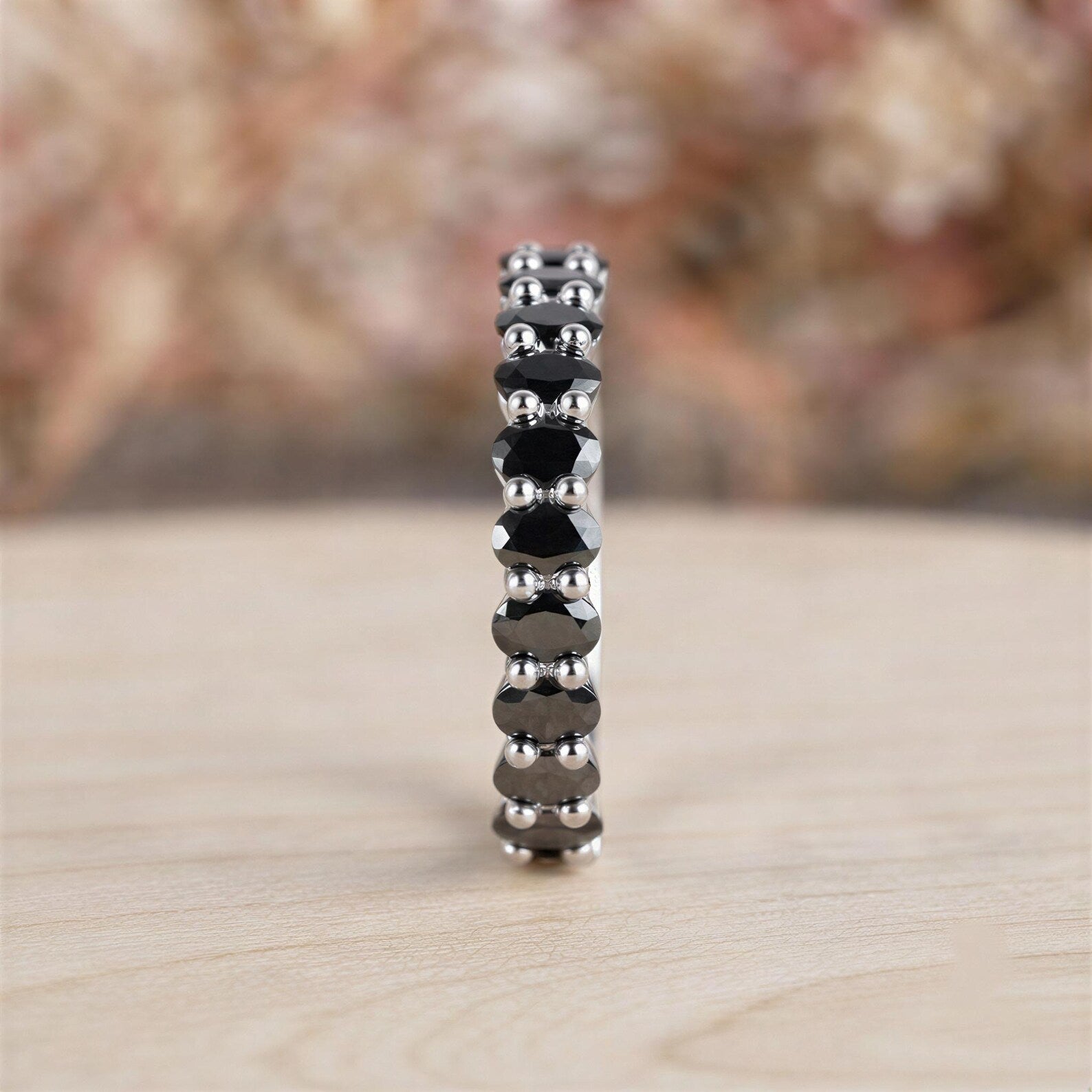 A silver ring with a row of black diamonds on a wooden surface.