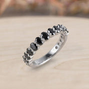 A silver ring with a row of black diamonds set in a light-colored metal band.