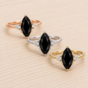 Three rings with black diamonds and gemstones are displayed on a wooden surface.