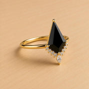 A gold ring with a large black gemstone, possibly a diamond, and a smaller diamond accent, set in a gold band.