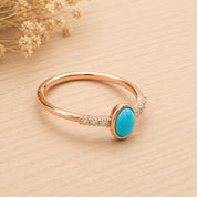 A gold ring with a turquoise stone set in the center, surrounded by small diamonds, placed on a wooden surface.