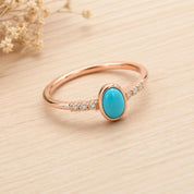 A rose gold ring with a turquoise stone set in the center, surrounded by small diamonds.