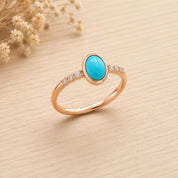A gold ring with a turquoise stone set in the center, surrounded by small diamonds, placed on a wooden surface.