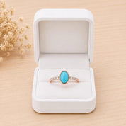 A white jewelry box containing a ring with a turquoise stone.