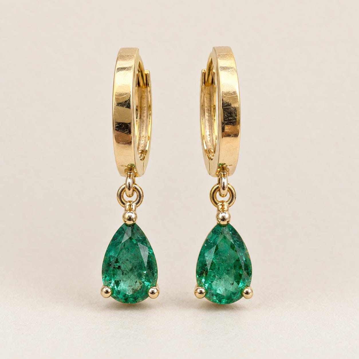 Pair of pear cut Zambian emerald drop huggie earrings in 14K yellow gold, front view