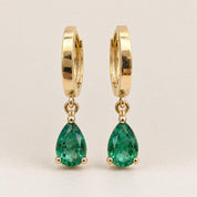 Pair of pear cut Zambian emerald drop huggie earrings in 14K yellow gold, front view